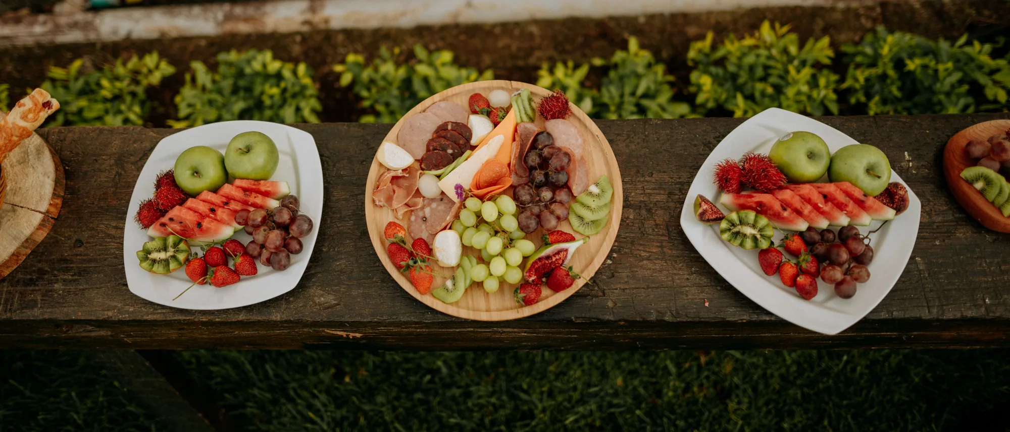 Tablas de fruta de la región y charcutería servidas sobre un tablón de madera en el jardín