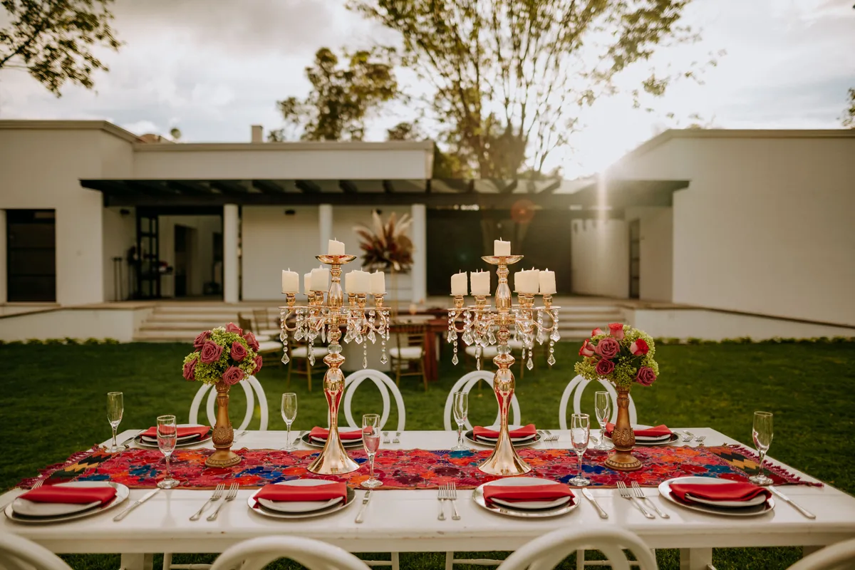 Mesa blanca vestida con textil mexicano bordado y candelabros dorados a contraluz