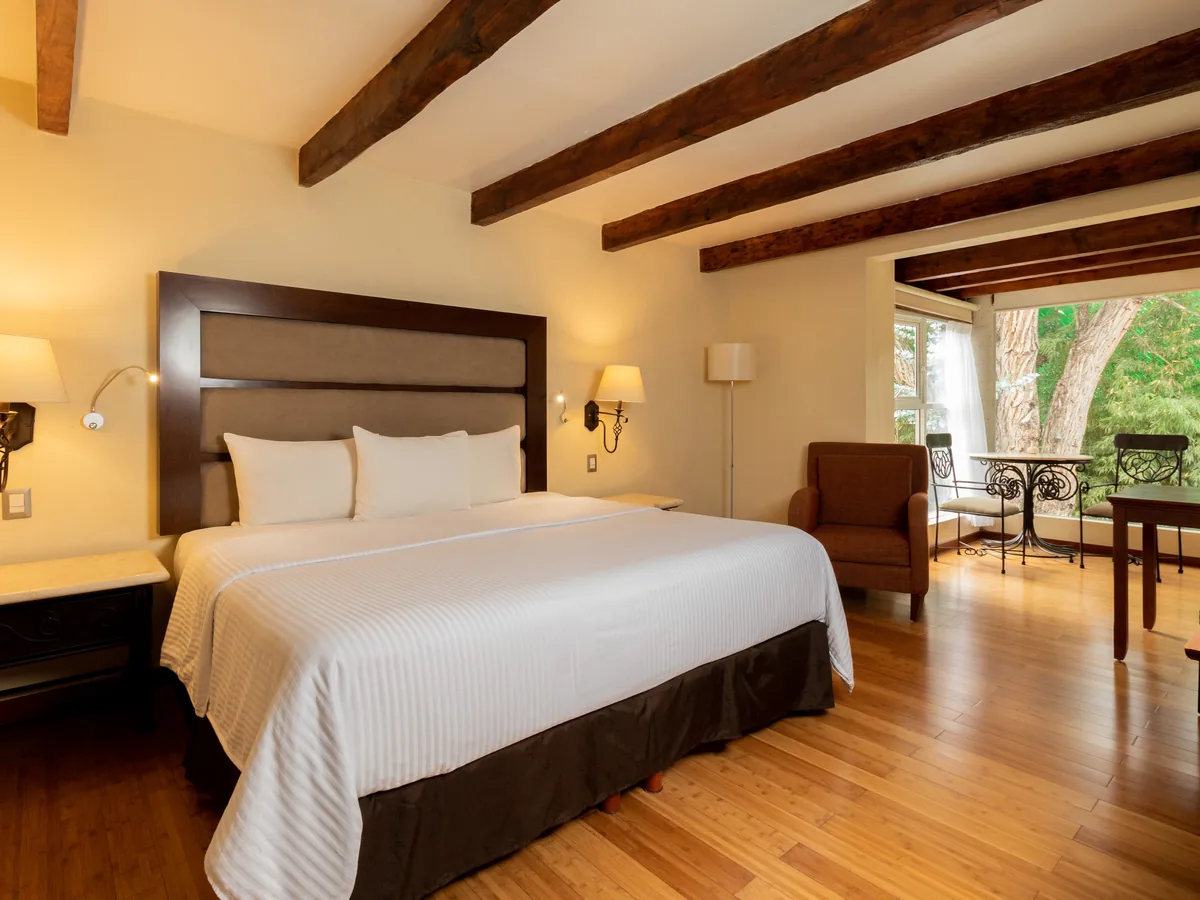 Junior Suite con cama king y la sala de estar al fondo, bajo vigas de madera